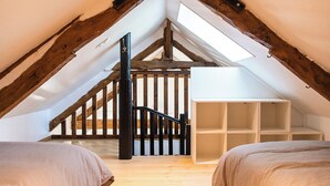 An attic bedroom with a sloped ceiling, wooden beams, a staircase, and built-in shelving. - Gîte on a farm with animals, near Arromanche-les-bains, 2 km from the sea (Ryes)