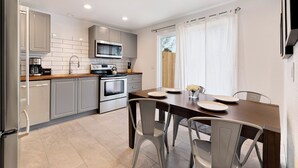 Una cocina moderna con armarios blancos, un microondas integrado y una estufa. Hay una mesa de comedor con sillas y una ventana con cortinas.