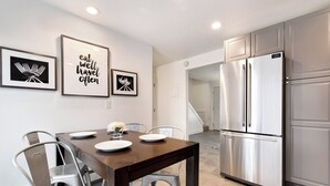 Una cocina moderna con electrodomésticos de acero inoxidable, una mesa de comedor con sillas y citas inspiradoras enmarcadas en la pared.