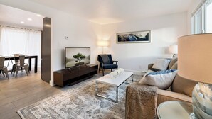 Una sala de estar moderna con una televisión de pantalla plana, un sofá, una mesa de centro y un comedor con sillas.