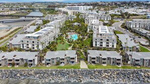 A modern residential complex with multiple apartment buildings, a central swimming pool, and a bridge in the background.