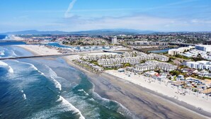 An aerial view of a coastal resort area with beachfront hotels, a marina, and a beach.