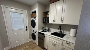 Une cuisine compacte équipée d’un lave-linge et d’un sèche-linge intégrés, d’un évier et de meubles de rangement blancs.