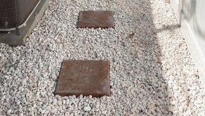 Un chemin menant à une maison avec une clôture blanche, un bâtiment bleu et un appareil de climatisation.
