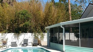 Une piscine dotée d’un patio couvert, entourée d’arbres et bordée d’un mur blanc.