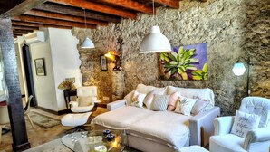Un salon chaleureux avec un mur en pierre, un canapé blanc, une table basse en verre et un fauteuil blanc.