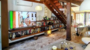 Un salon confortable avec un téléviseur, des étagères à livres, une table basse et un escalier.