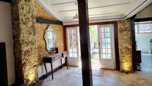 Une pièce aux murs de pierre, au plafond en bois et dotée d’un grand miroir. On y trouve une porte donnant sur l’extérieur ainsi qu’une petite table sur laquelle est posé un vase.