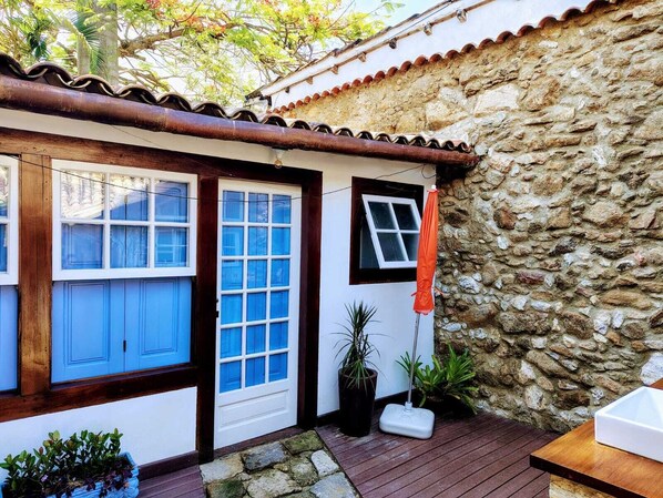 A rustic building with a stone wall, a wooden deck, and a small patio area with potted plants.