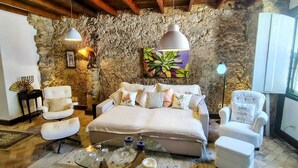 Une pièce chaleureuse avec un mur en pierre, un lit, deux chaises, une table basse en verre et des lampes suspendues.