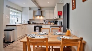 A modern kitchen with white cabinets, a stainless steel range hood, and a dining table set with plates, glasses, and a pitcher of orange juice.