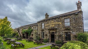 The Wellington Inn, a stone building with a sign, outdoor seating, and a grassy area.