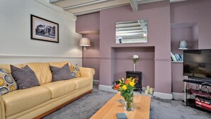 A living room with a beige sofa, a wooden coffee table with a vase of flowers, a fireplace, a television, and a framed picture on the wall.