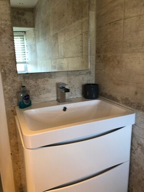 Bathroom features a sink and mirror, with a stone-patterned wall and a hand soap dispenser.