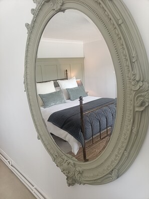 A bedroom with a large ornate mirror, a bed with a dark quilt, and a headboard against a plain wall.
