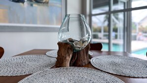 A glass sculpture on a wooden stand, surrounded by woven placemats on a table with a view of a swimming pool through large windows.