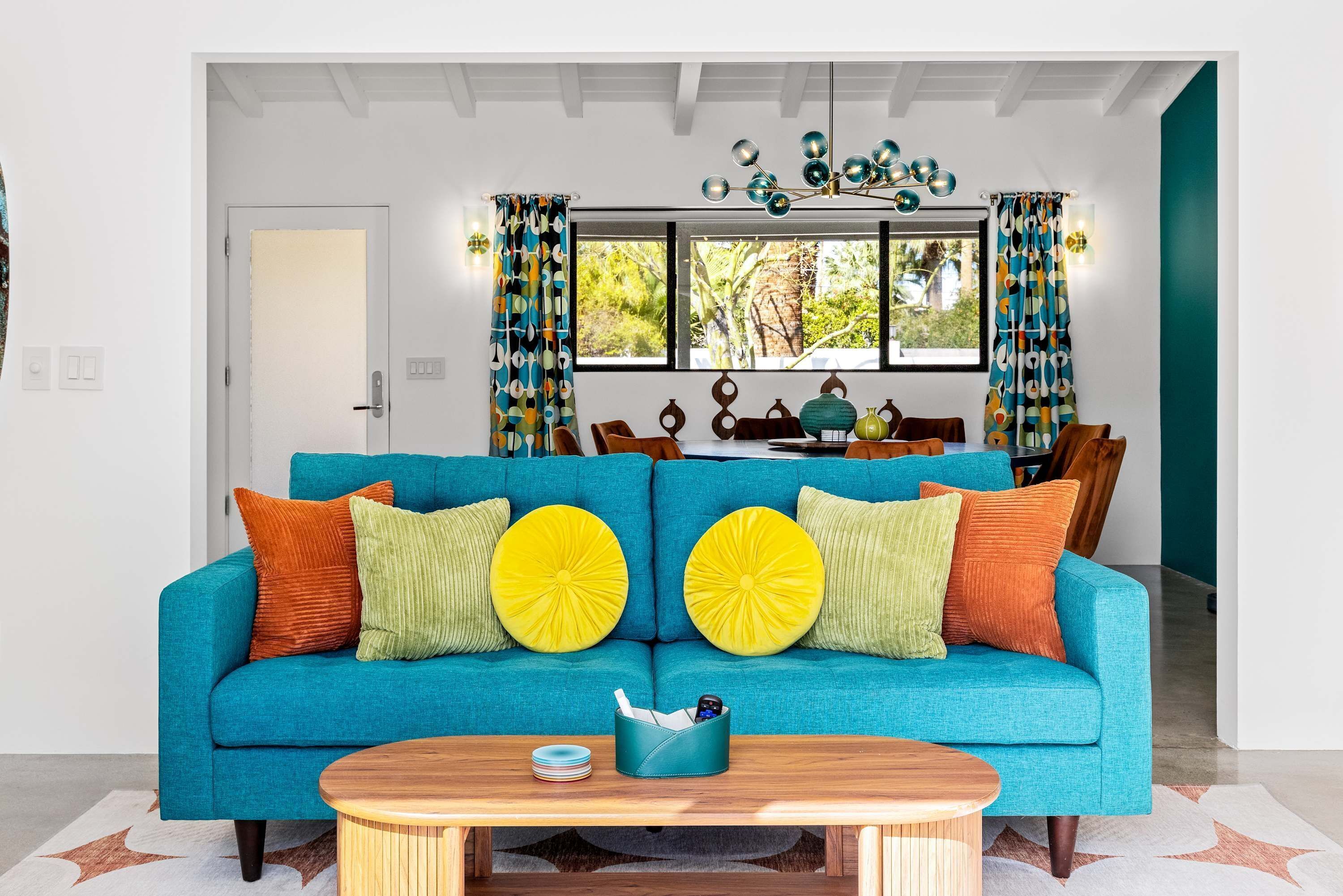 A living room with a teal sofa, wooden coffee table, and a dining area with a wooden table and chairs.