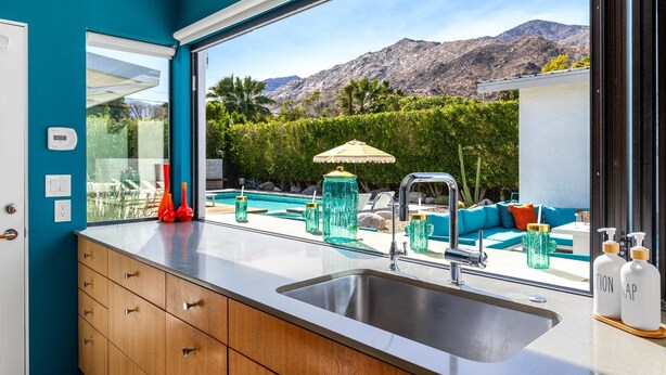 A modern kitchen with a large window, a stainless steel sink, and a view of a pool and mountains. - Luxury 4-bedroom Home With Pool Spa Stunning Mountain Views (Palm Springs)