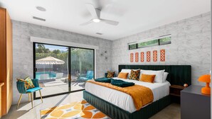 A modern bedroom with a large bed, a ceiling fan, and a view of an outdoor pool area. - Luxury 4-bedroom Home With Pool Spa Stunning Mountain Views (Palm Springs)