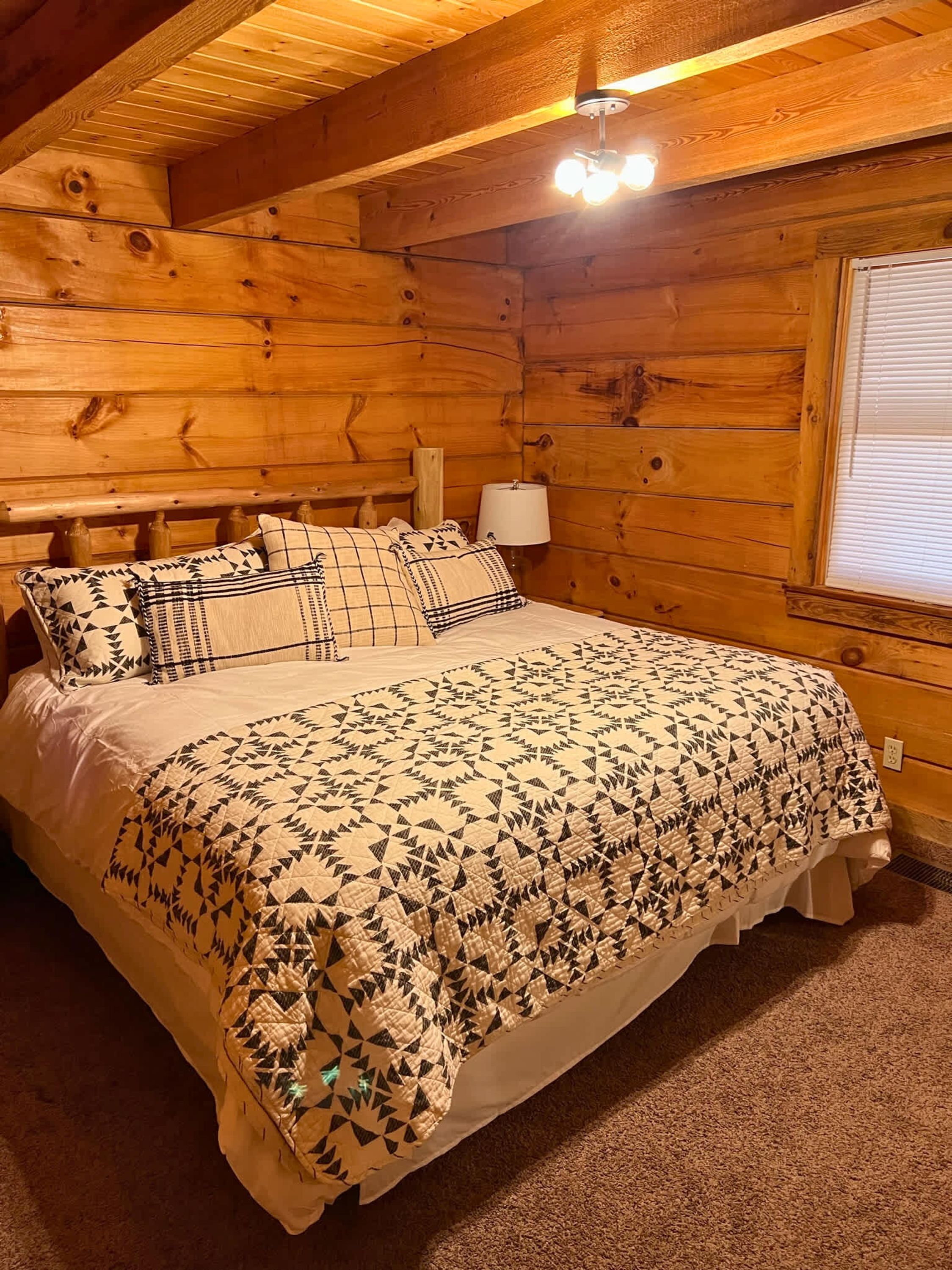 A wooden cabin bedroom with a bed, pillows, a nightstand, and a window.
