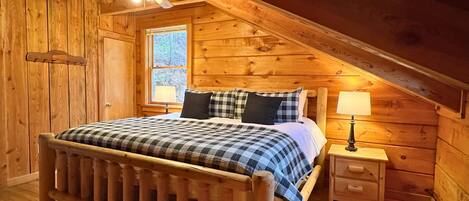 Un dormitorio de cabaña de madera con una cama, dos mesitas de noche, una ventana y un ventilador de techo.