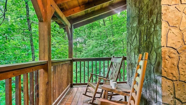 A wooden deck with a stone wall and a view of a forest. - Hunter Hills Haven - Secluded Luxe Cabin Getaway With Mountain Views Spa Hot Tub Game Room (Sevierville)