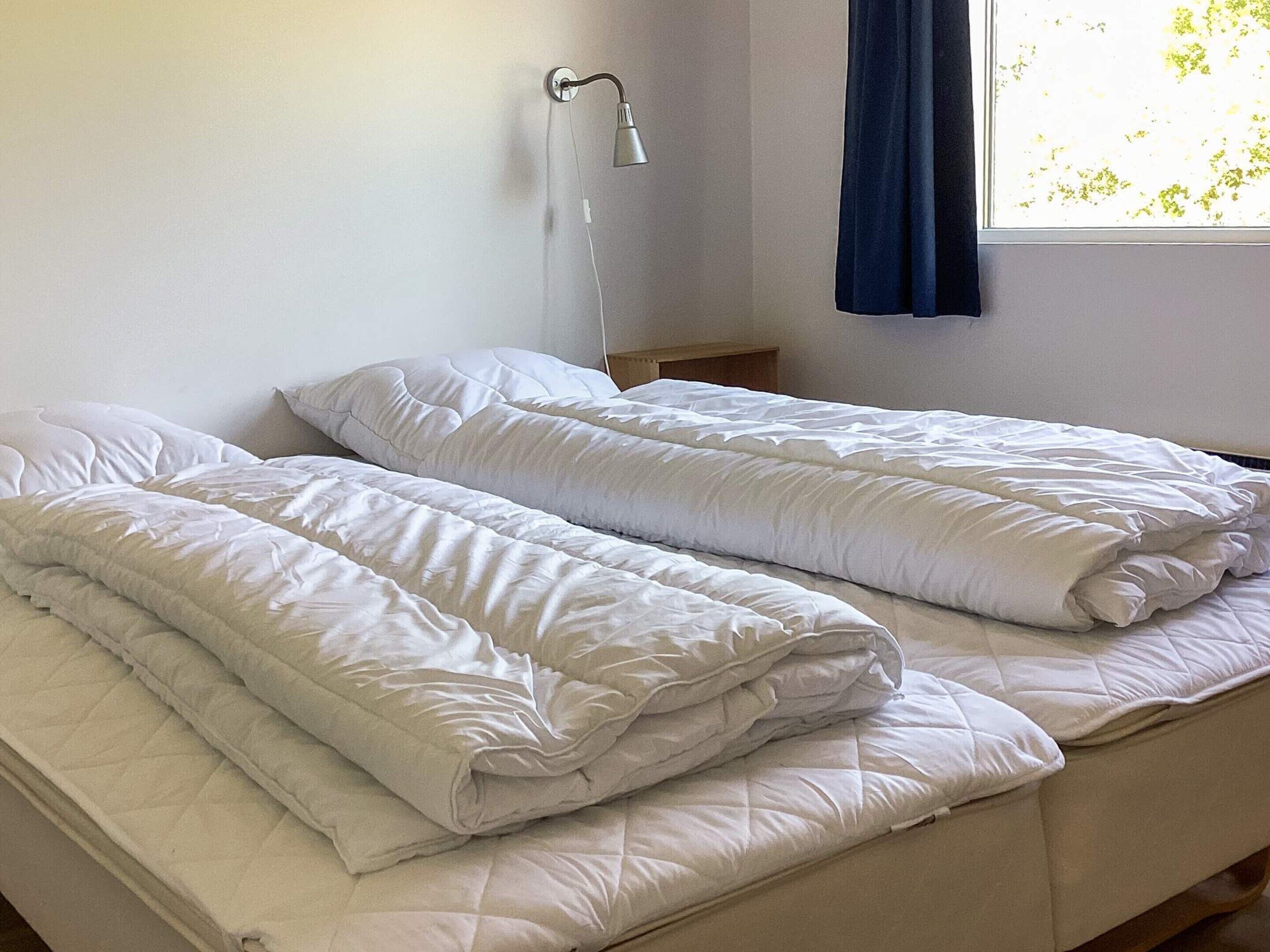 Un lit simple avec une literie blanche, une table de chevet et une lampe fixée au mur.