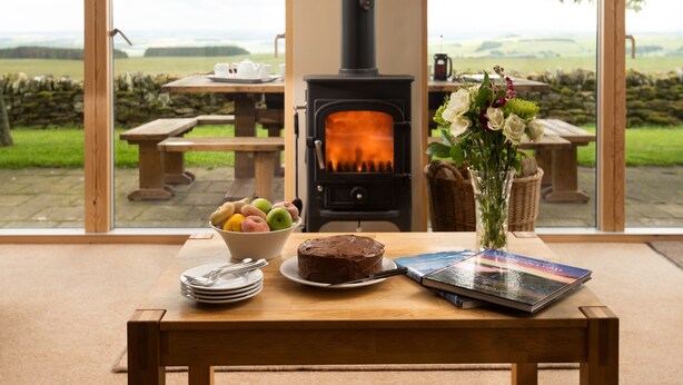 A cozy room with a wooden table, a cake, a bowl of fruit, and a vase with flowers. - Two self catering holiday homes that sleeps 14 guests  in 7 bedrooms (Hexham)