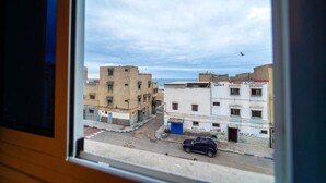 A view from a window of a street with buildings, a parked car, and a bird in the sky. - Anza Sets House  (Anza)