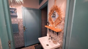 A bathroom with a white sink, a mirror with a decorative frame, and patterned wallpaper. - Anza Sets House  (Anza)