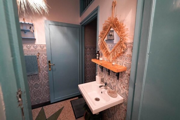 A bathroom with a white sink, a mirror with a decorative frame, and patterned wallpaper. - Anza Sets House  (Anza)