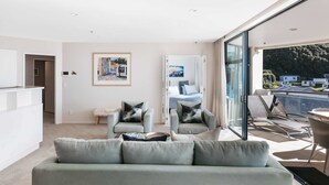 Un salon moderne avec un canapé gris, deux fauteuils et une porte vitrée donnant sur un balcon aménagé avec des sièges d’extérieur.