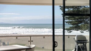 Une vue depuis un balcon donnant sur une plage, avec des vagues, une chaise et un vélo.