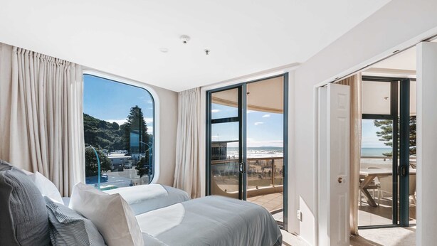 Une chambre dotée d’une grande fenêtre, d’un lit et d’une porte-fenêtre coulissante donnant sur un balcon avec vue sur la plage.