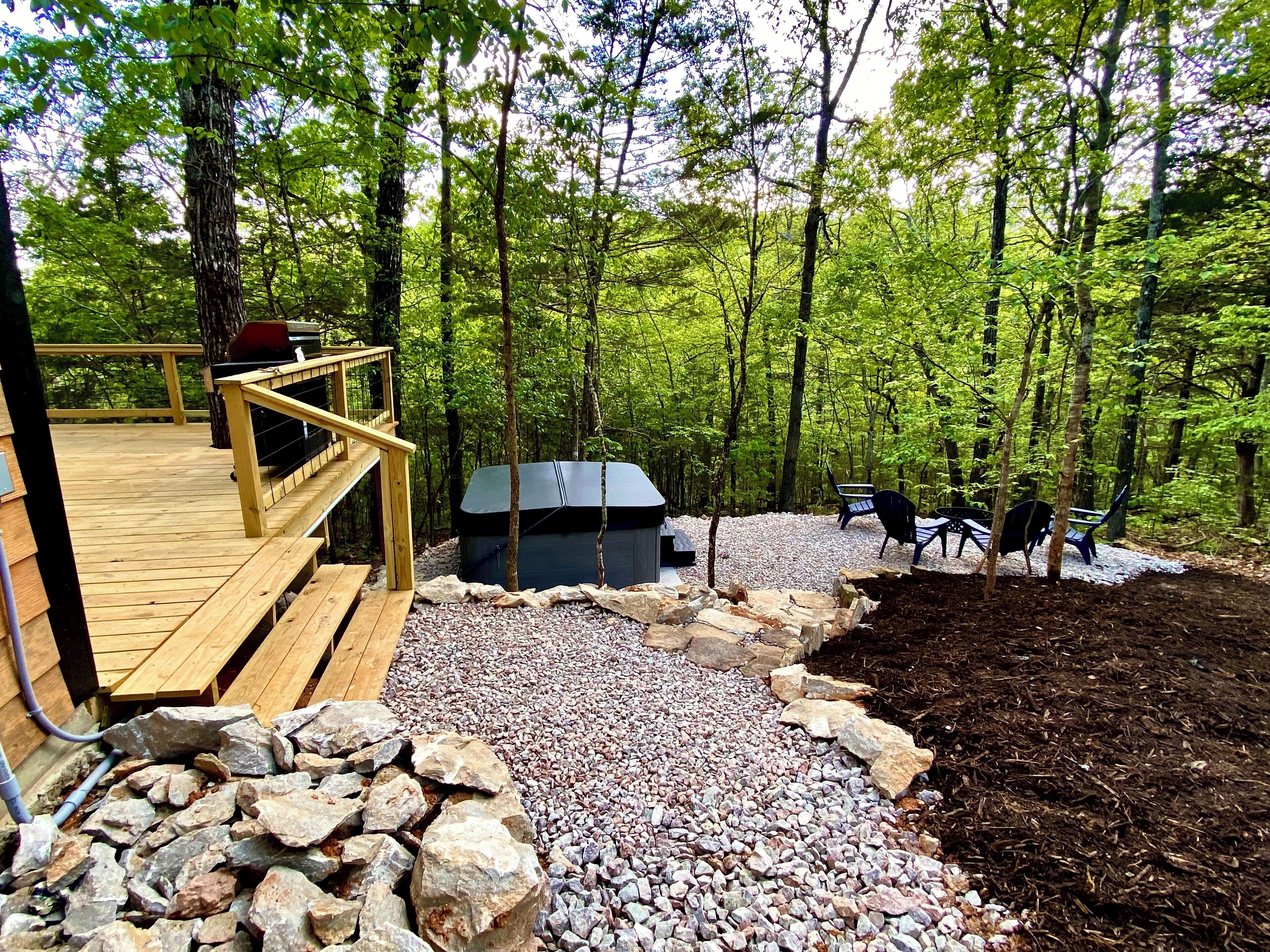A wooden deck with a hot tub, surrounded by a forest.