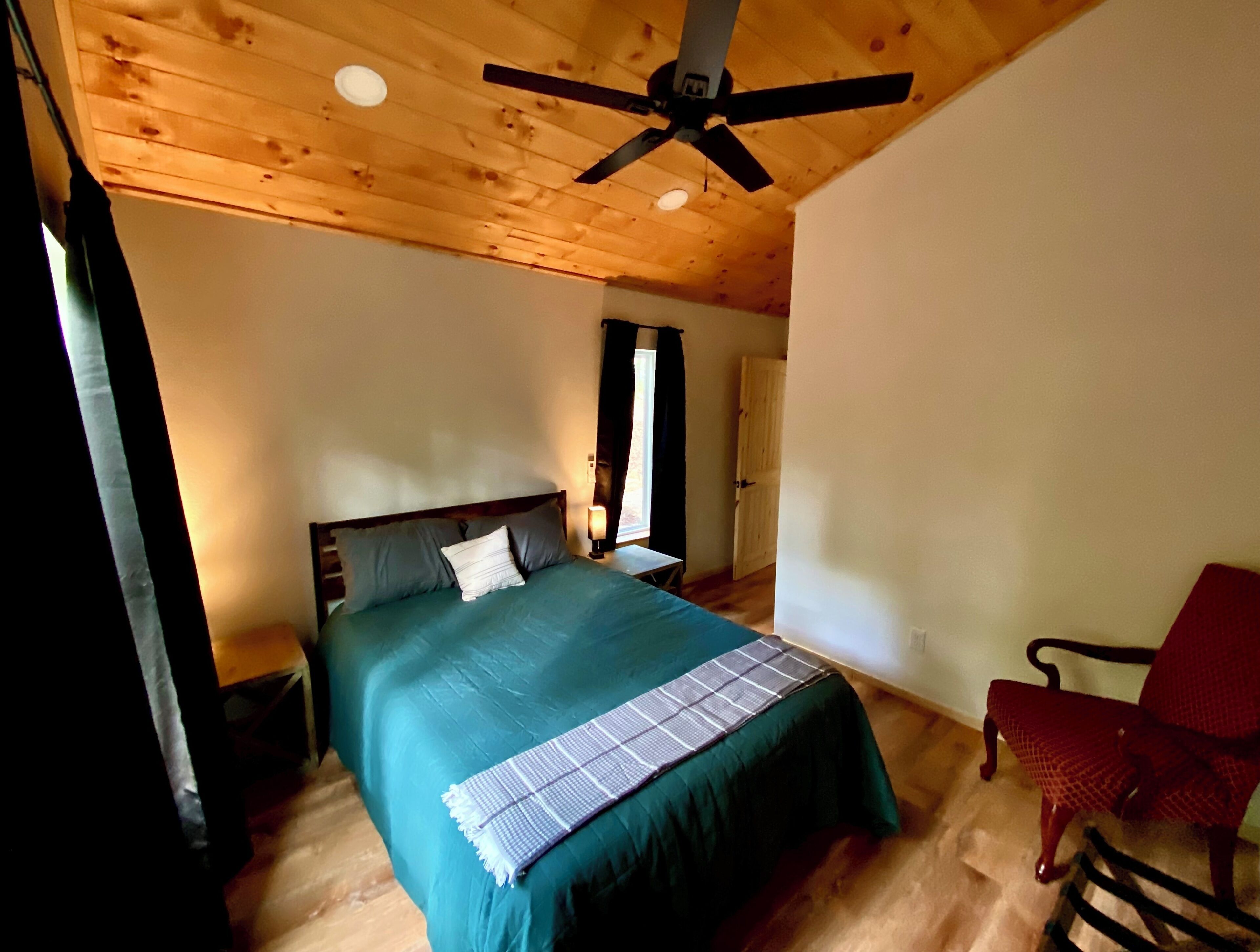 Een slaapkamer met een bed, een plafondventilator, een raam en een stoel.
