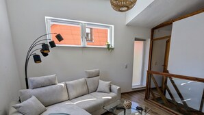 A modern living room with a sofa, a glass coffee table, and a view of a red brick building through a window.
