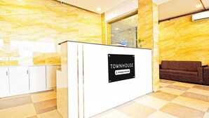 Un'area di accoglienza con una parete in marmo, una reception con la scritta 'TOWNHOUSE Company Serviced', un divano e un pavimento piastrellato.