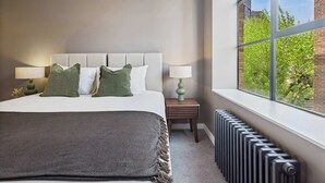 A modern bedroom with a large bed, two bedside tables, and a view of greenery through a window.