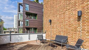 A rooftop terrace with wooden flooring, metal chairs, and a brick wall.