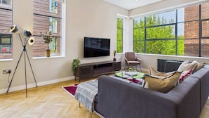 A modern living room with a large window, a flat-screen TV, a sofa, a chair, and a floor lamp.