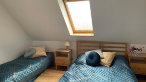 Une chambre avec deux lits, un puits de lumière et une table de chevet avec une lampe.