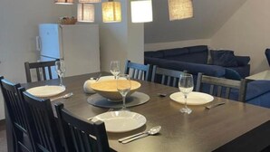 Un coin repas avec une table ronde dressée pour quatre personnes, entourée de chaises noires. Des lampes suspendues à texture tissée sont placées au-dessus de la table.
