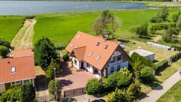 Un bâtiment avec un toit recouvert de tuiles rouges, une enseigne indiquant un restaurant, et une vue sur un lac où l’on peut apercevoir des bateaux.