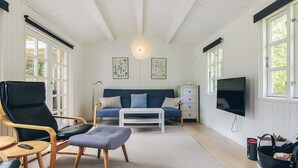 A room with a sofa, a chair, a coffee table, a TV, and a window. - 6 Person Holiday Home in Gedser (Gedser)