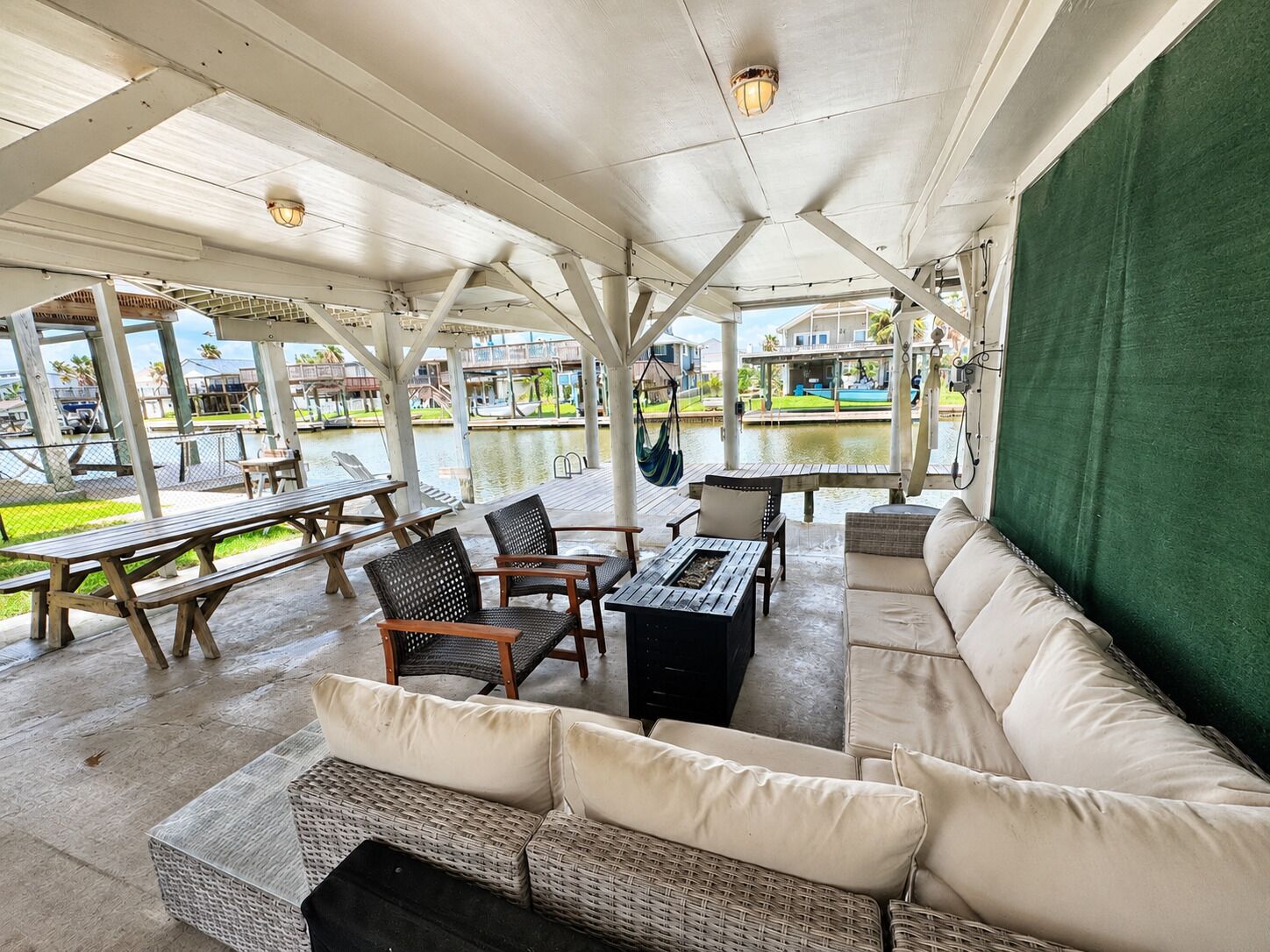 Eine überdachte Terrasse im Freien mit Sitzgelegenheiten, Tischen und Blick auf ein Gewässer.