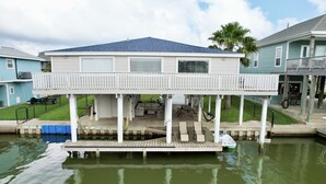 A waterfront house with a covered deck, a boat dock, and a small boat.