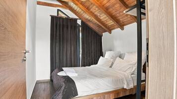 Una camera da letto con soffitto spiovente, un letto con biancheria bianca e una tenda scura.