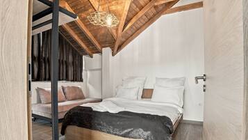 Ein Schlafzimmer mit schrägen Wänden, einem Bett mit weißer Bettwäsche, einem dunkelgrauen Sofa und einer hängenden Deckenleuchte.