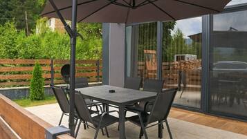 Eine Terrasse im Freien mit Tisch, Stühlen, einem großen Sonnenschirm und einer hölzernen Bank.
